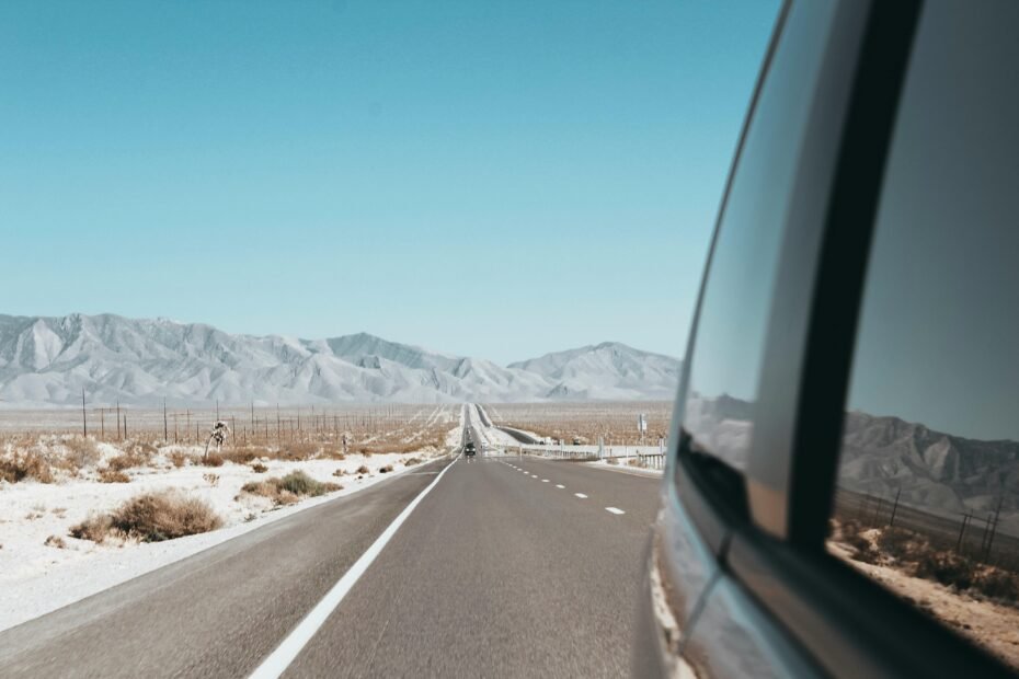 A car on a scenic highway driving towards a stunning American mountain range at sunset, an example of the top places to visit in the US.