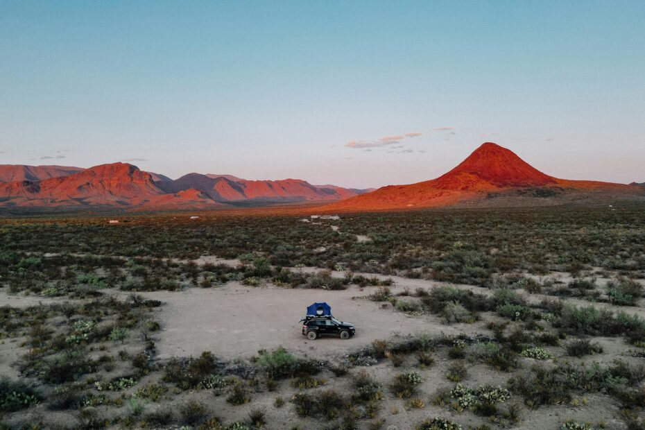 A scenic road winds through the vast Texas desert landscape towards mountains at sunset, symbolizing the adventure of exploring tourist places in the Lone Star State.