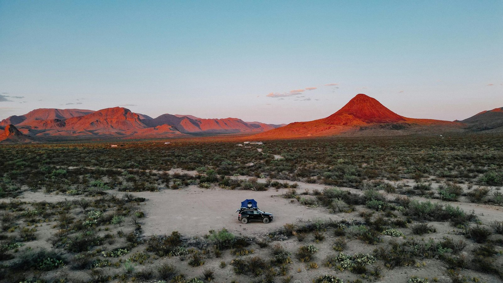 A scenic road winds through the vast Texas desert landscape towards mountains at sunset, symbolizing the adventure of exploring tourist places in the Lone Star State.