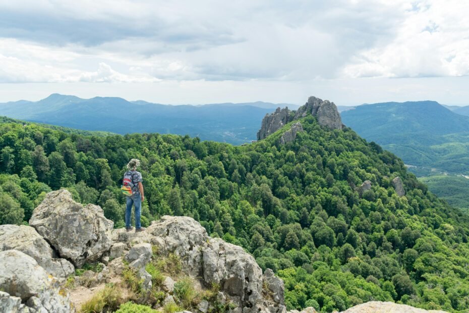 A solo traveler with a backpack looks out over a stunning mountain range, feeling empowered and ready for an adventure after reading these essential solo travel tips.