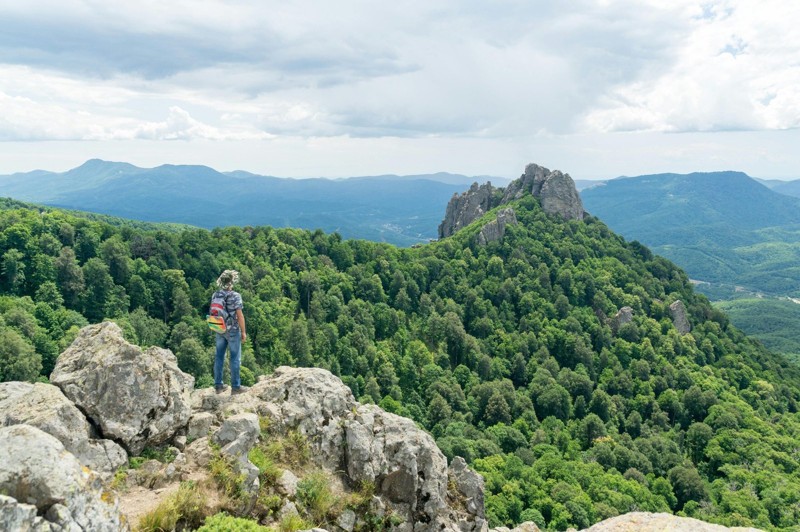 A solo traveler with a backpack looks out over a stunning mountain range, feeling empowered and ready for an adventure after reading these essential solo travel tips.