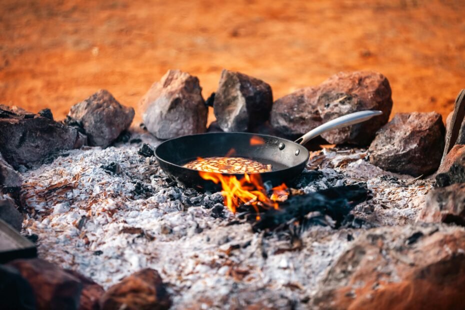 One of the best camping meals being cooked in a cast iron skillet over a glowing campfire at a forest campsite.