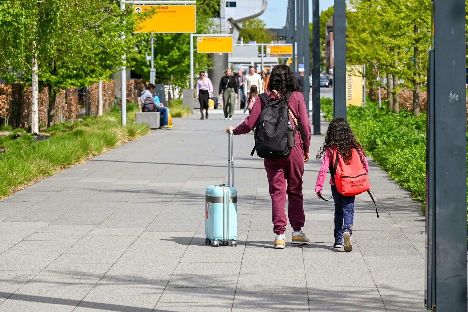 Parent smiling, pushing baby in a lightweight, compact travel pushchair through a busy airport terminal, highlighting stress-free family travel and adventure.