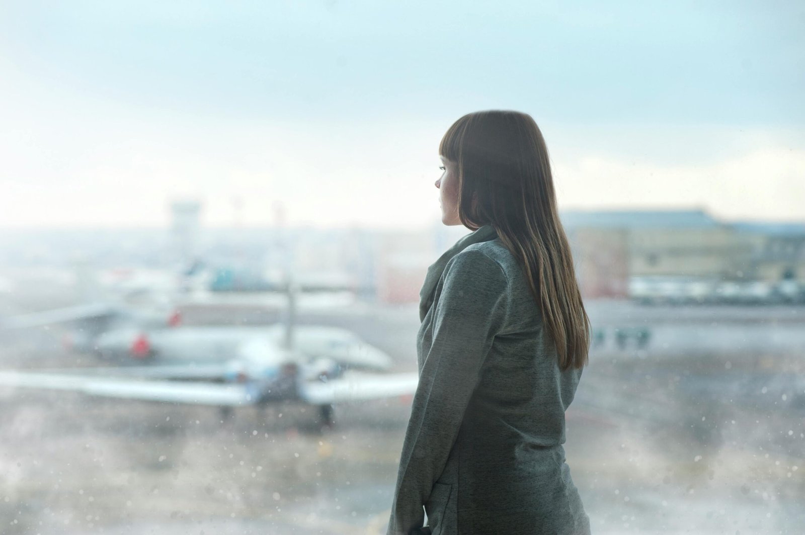 A confident first-time flyer holding a passport looks out an airport window at a plane on the tarmac, ready for their trip.