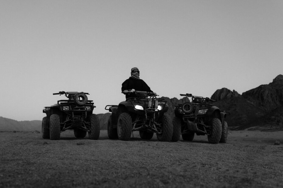 A group of people enjoying an exciting Mojave Desert ATV tour, riding their vehicles down a sandy trail with scenic red rock formations in the background.