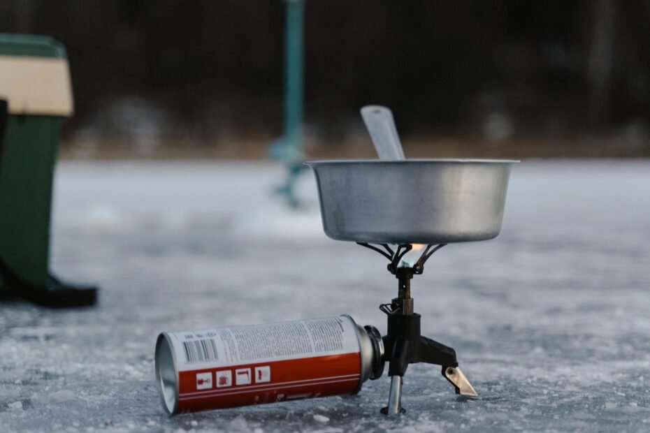 A compact single burner propane stove in use, heating a pot during a camping trip in the woods.
