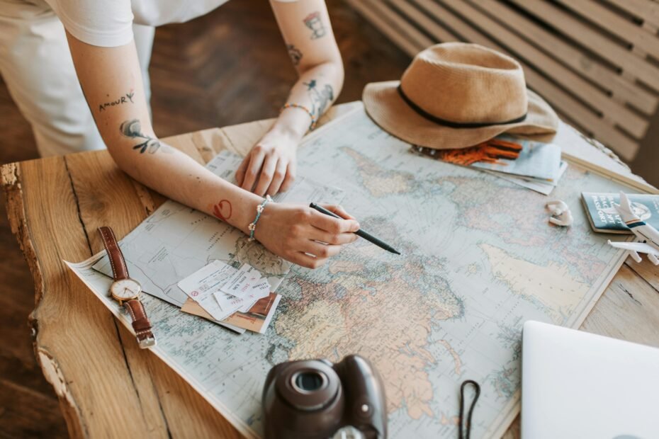 A person's hands tracing a route on a world map next to a notebook, illustrating the process of planning and budgeting to learn how to travel more.