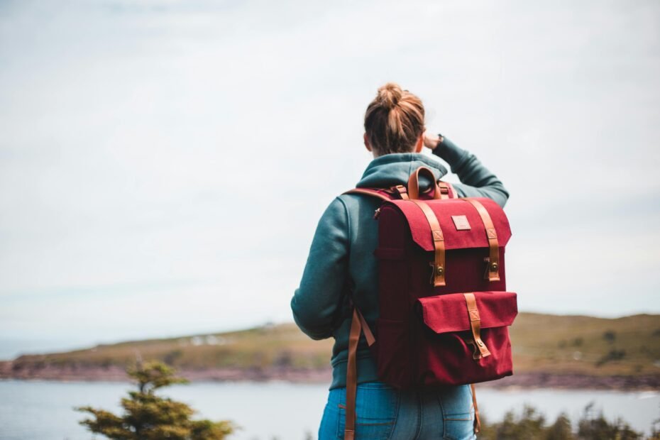 A solo traveler with a backpack stands on a mountain top looking out at the view, representing the freedom and self-discovery of a solo travel trip.