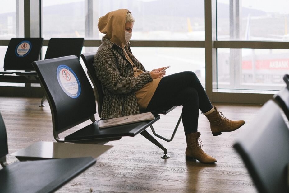 Person wearing a stylish and functional travel hoodie with multiple pockets and comfort features, relaxing in an airport setting, emphasizing comfortable and organized travel.
