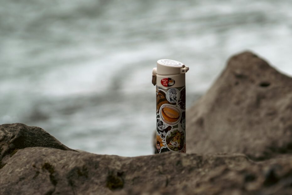 Reusable stainless steel travel water bottle against a blurred scenic landscape, symbolizing sustainable travel and essential hydration for modern adventurers.