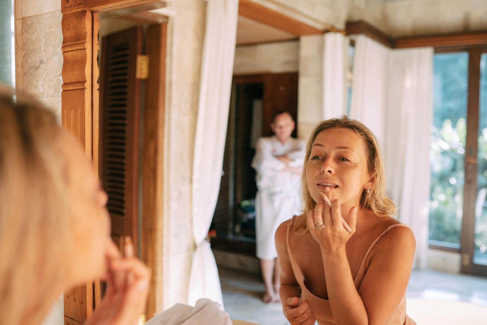 Woman using an illuminated travel magnifying mirror for precise makeup application in a modern hotel room, showcasing consistent bright LED lighting and portable convenience for flawless grooming while traveling.