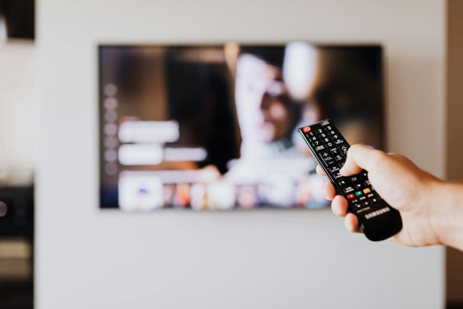 Hand holding a remote control, navigating a TV guide on a screen to find the latest Travel Channel schedule for paranormal and mystery shows.