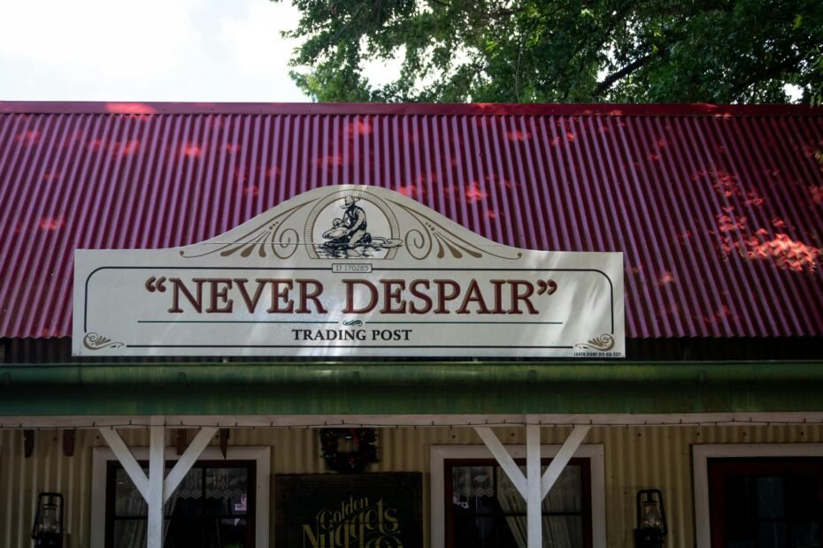 A post-apocalyptic merchant standing inside a rustic trading shack on a trailer at a safe zone outpost, surrounded by various valuable survival items and components, ready to trade for scrap.
