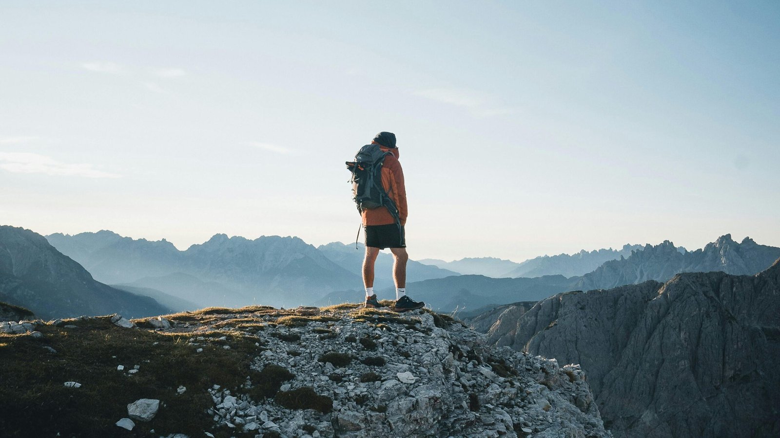A person wearing a huge travel backpack stands on a scenic overlook, symbolizing long-term adventure travel, freedom, and readiness for global exploration.