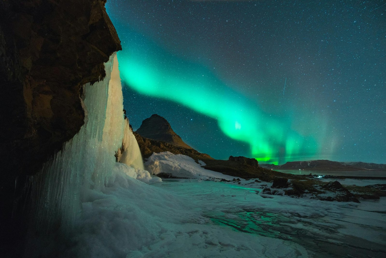 Vibrant green and purple Northern Lights (Aurora Borealis) intensely illuminating a vast, dark Icelandic winter night sky over majestic snow-capped mountains and a serene, untouched landscape, suggesting the optimal season for an unforgettable aurora hunting trip to Iceland.