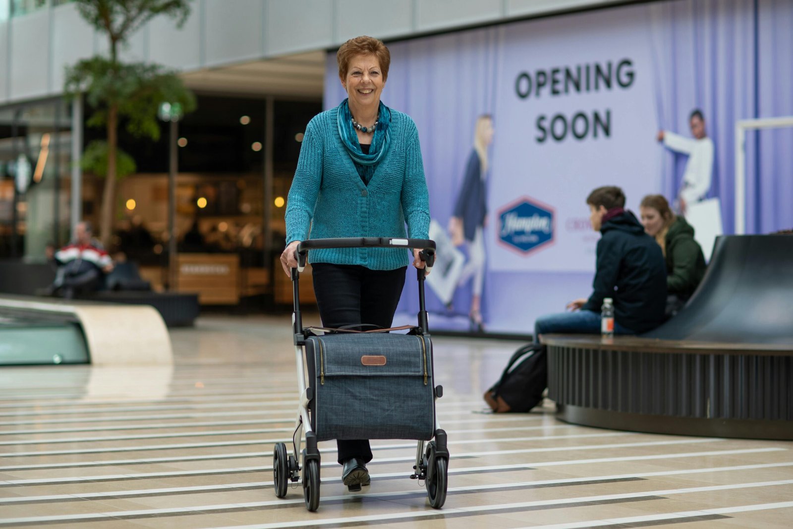 A smiling senior person using a modern, lightweight, foldable travel walker to move confidently through a bright airport terminal, symbolizing independence and active travel.