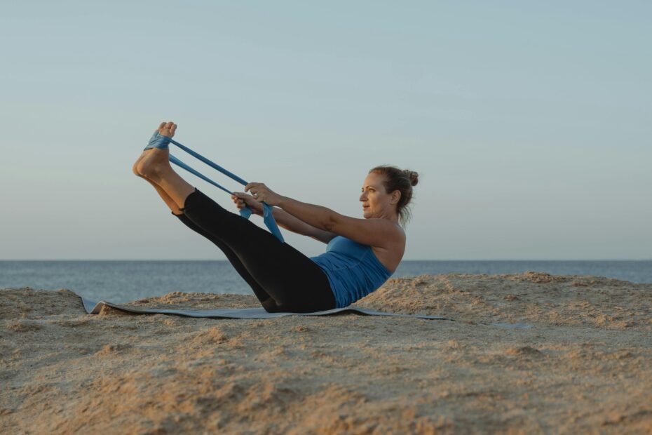 Woman in a peaceful yoga pose on a thin, foldable travel yoga mat on a beautiful beach at sunrise, symbolizing the freedom of portable yoga for travelers.