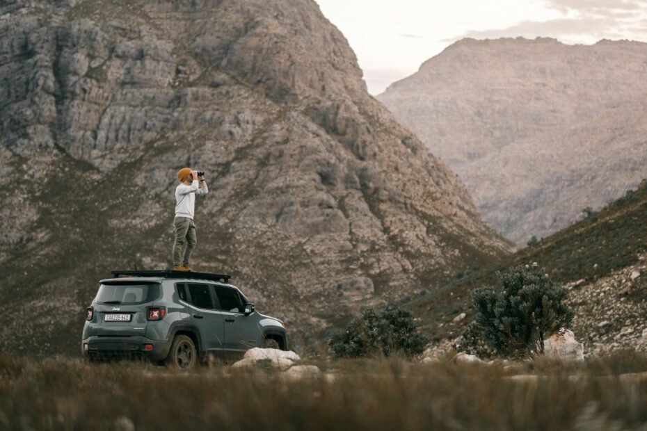 Traveler using compact binoculars to view a scenic mountain landscape, highlighting the enhanced experience of discovery and detailed observation.
