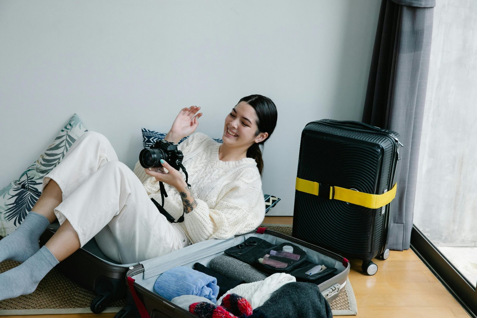 A smiling female traveler efficiently packing her suitcase with essential tech gadgets, comfort items, and stylish travel accessories, perfect for an adventurous and enjoyable journey. Ideal gifts for traveling women.