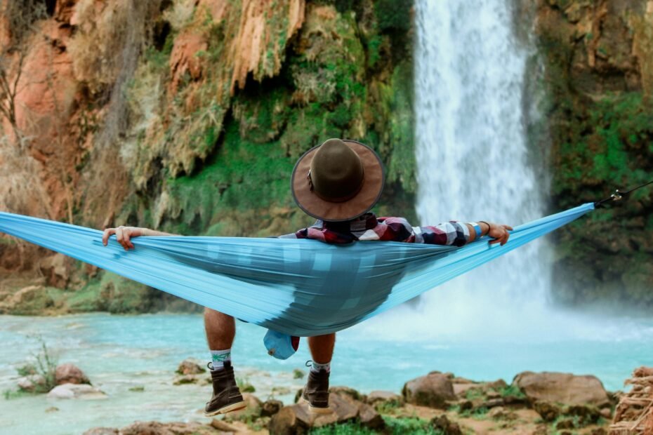Person relaxing in a colorful travel hammock suspended between trees in a serene forest, symbolizing outdoor comfort and adventure.