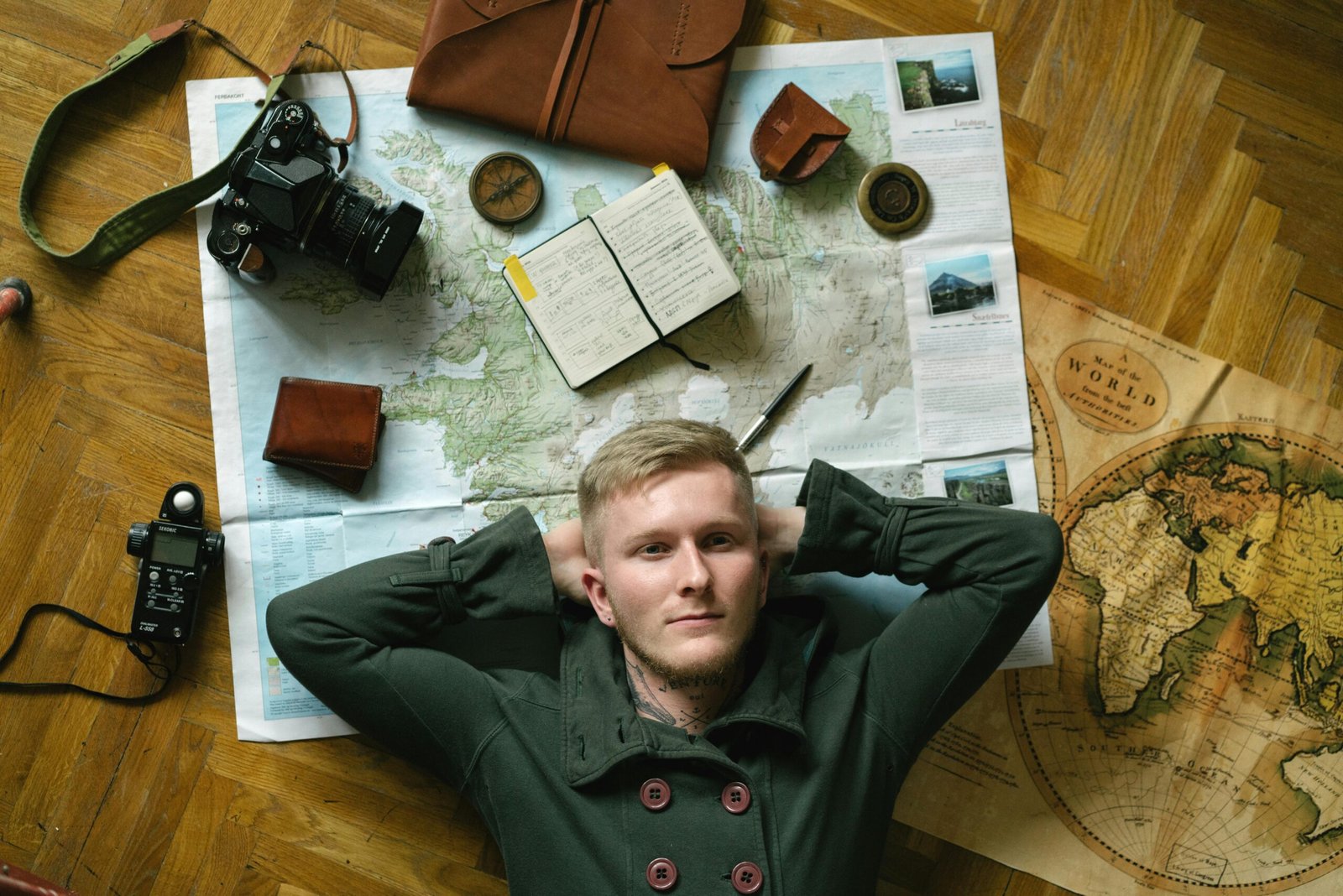 A stylish male traveler looking at a map with travel essentials and tech gadgets around him, representing thoughtful gifts for men who love adventure and exploring.