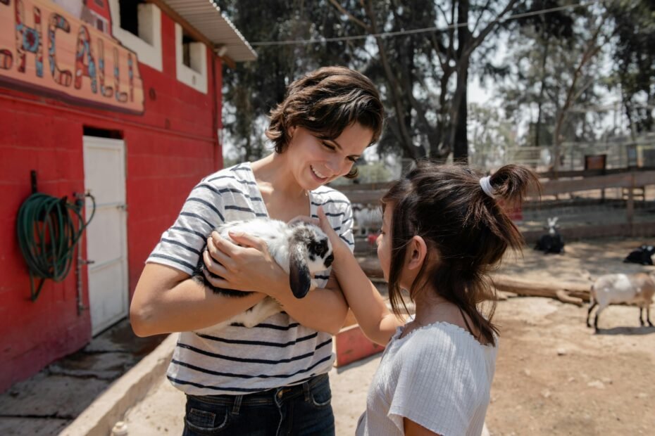 Happy children and families petting gentle miniature goats, rabbits, and ducks at a vibrant outdoor traveling petting zoo event, supervised by a friendly handler, perfect for parties and educational experiences.